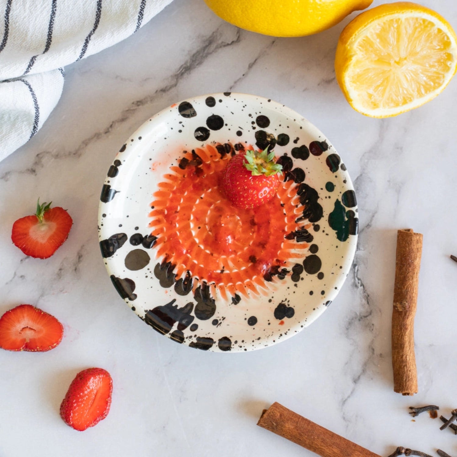 Speckled ceramic plate with strawberry and orange on a marble surface with lemons, strawberries, and cinnamon sticks.