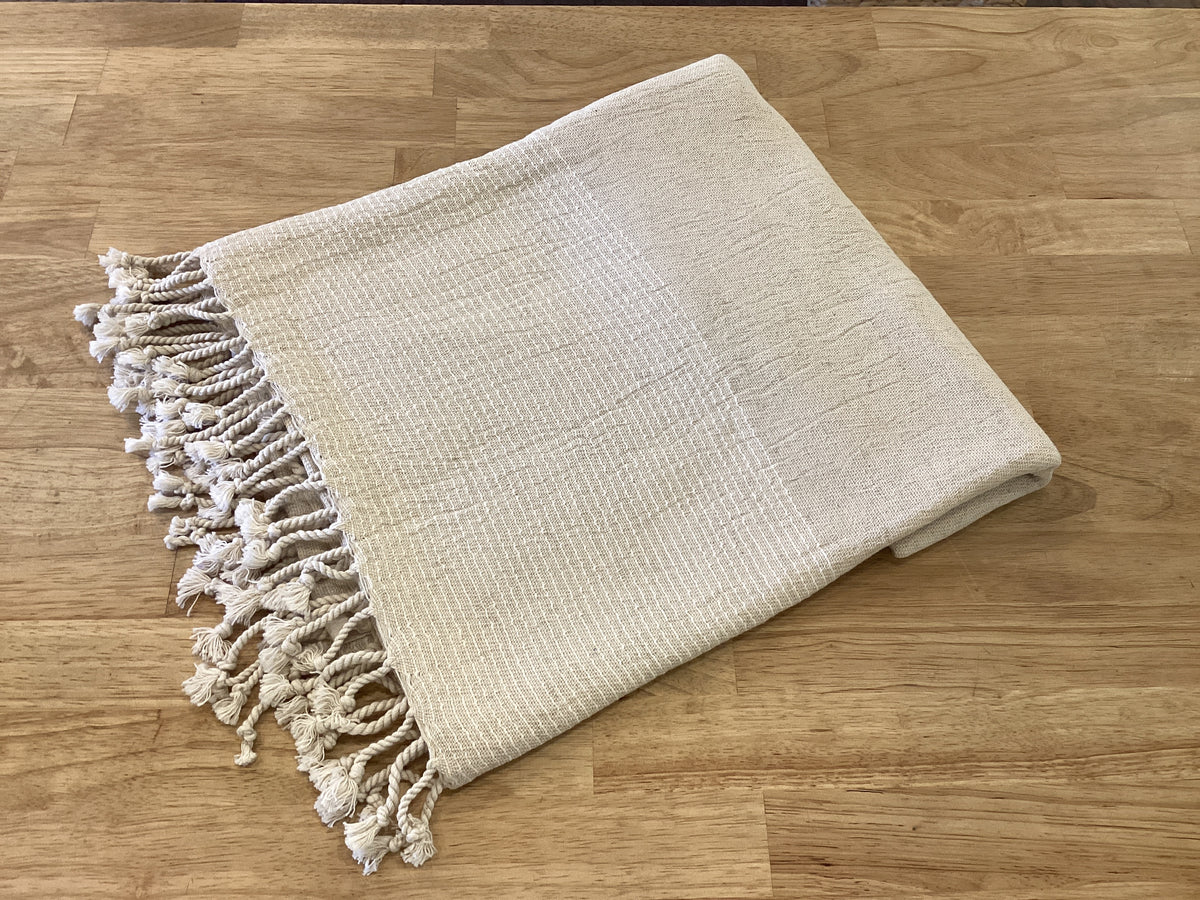 Lavender Road linen Turkish body towel draped over a wooden surface, showcasing its soft, textured fabric and natural color.