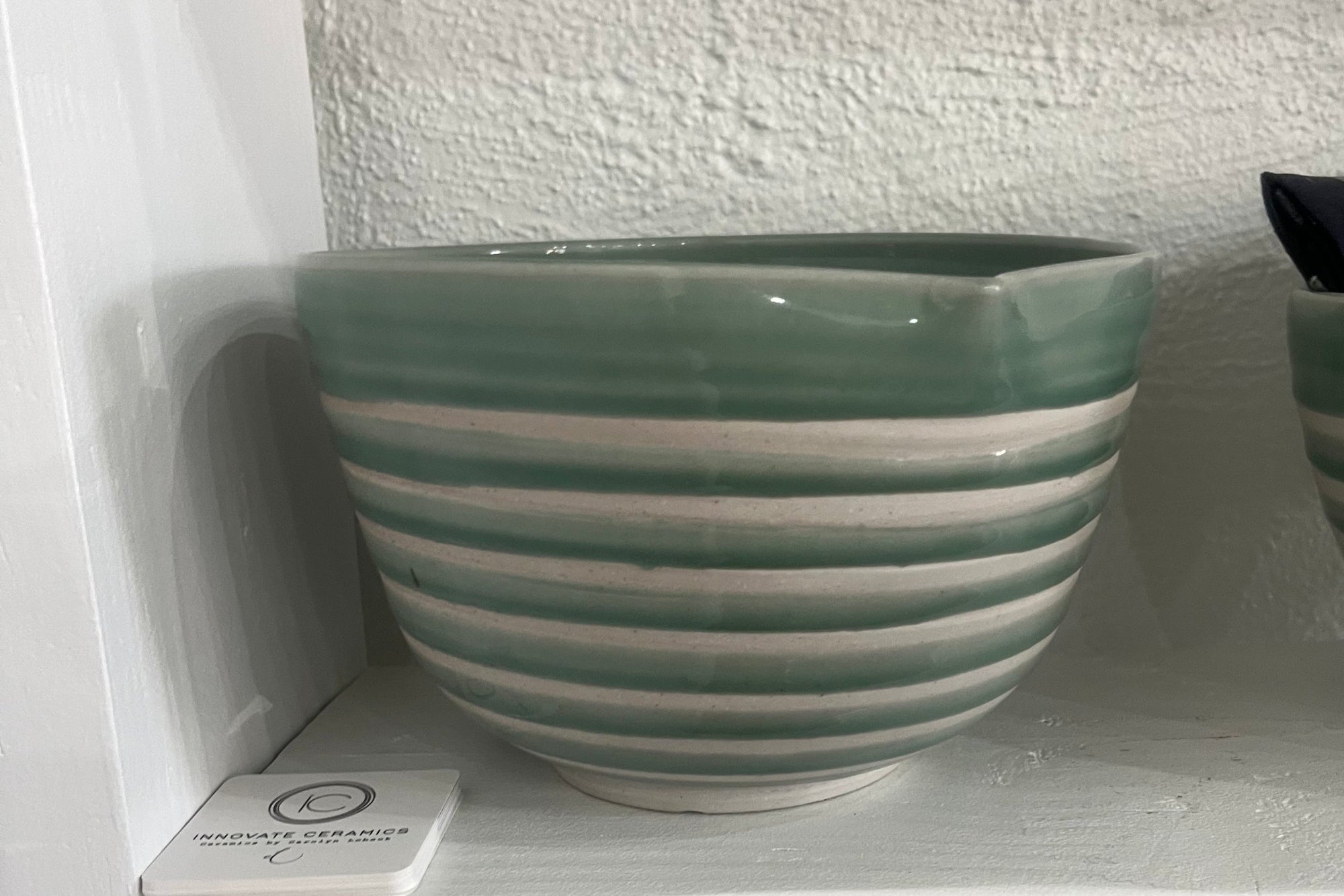 Green and white striped ceramic bowl on a white surface with a textured wall background.