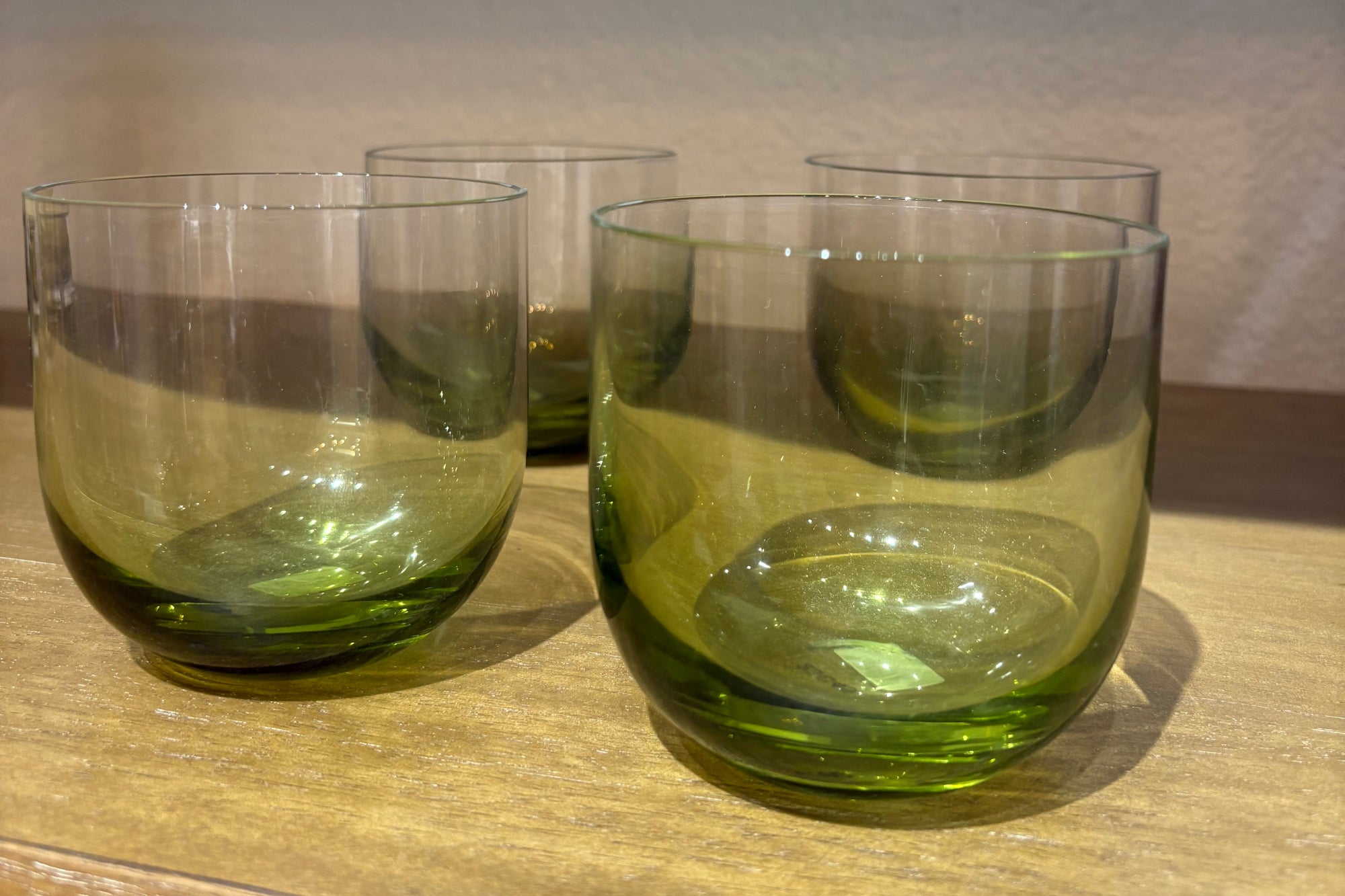 Four green glass tumblers on a wooden surface