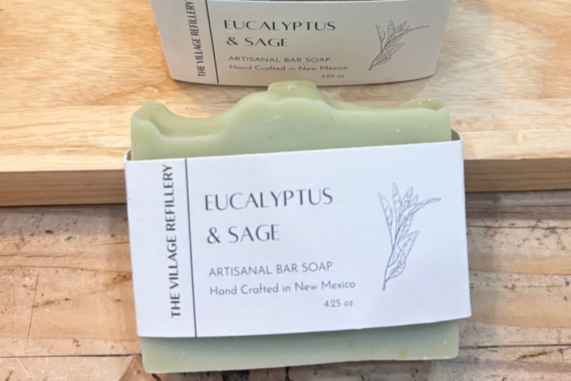 Two bars of Eucalyptus & Sage soap from The Village Refillery on a wooden surface.