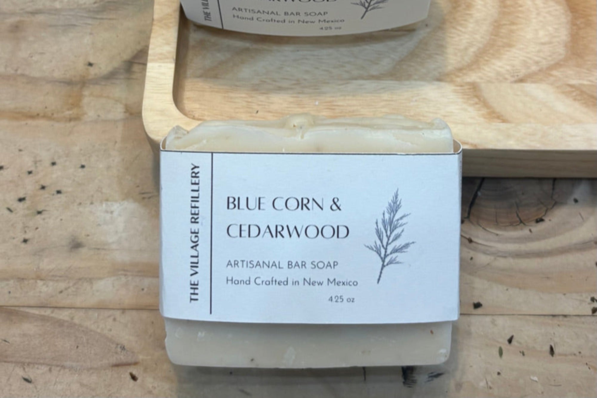 Two bars of Blue Corn & Cedarwood soap from The Village Refillery on a wooden surface.
