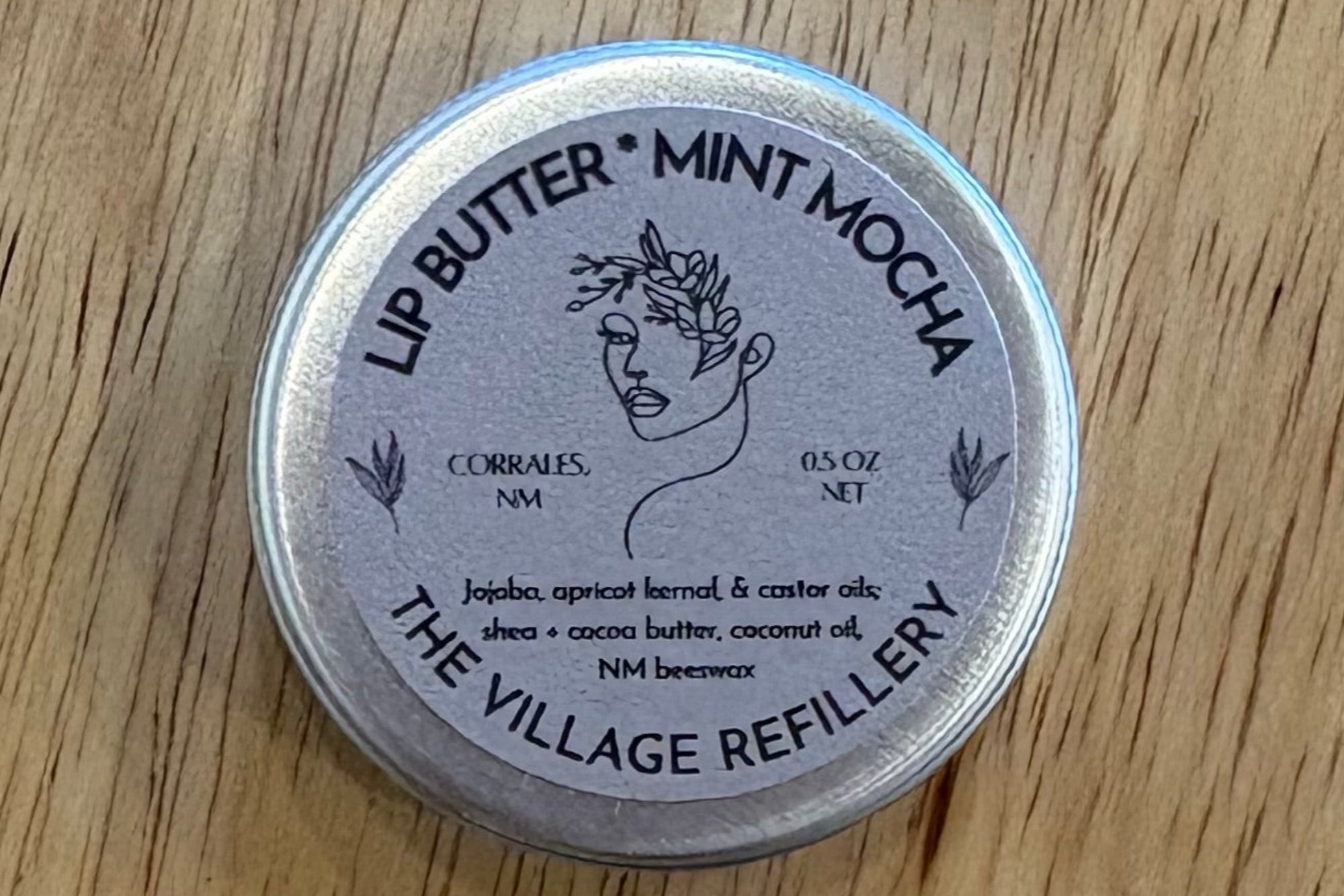 Lip butter container labeled 'Mint Mocha' from The Village Refillery on a wooden surface